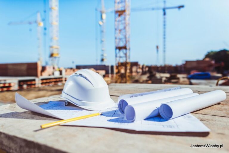 Biały kask ochronny i plany budowlane na placu budowy z dźwigami w tle